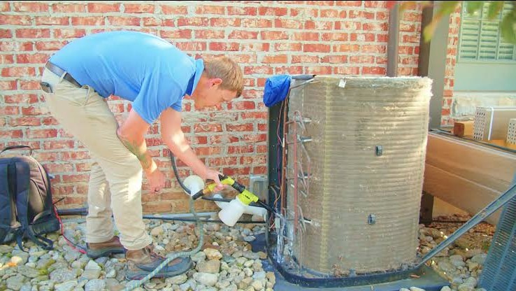 Technician cleaning pollen and debris from an HVAC condenser coil in Greensboro NC